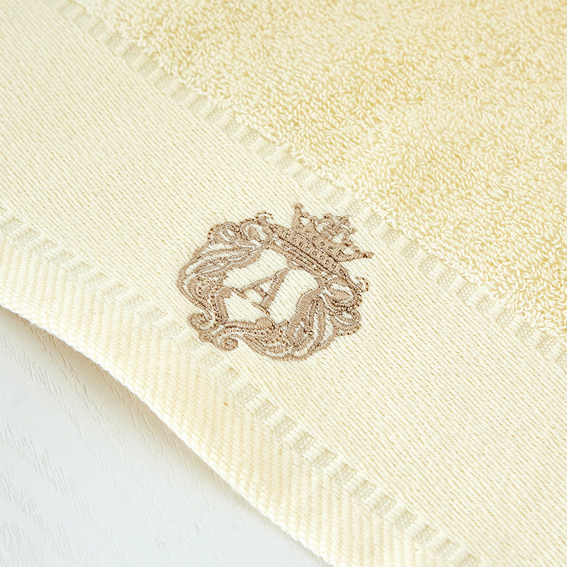 Close-up of Austin luxury bath towel embroidered crown crest detail in beige – premium cotton with elegant gold embroidery
